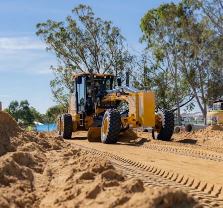 John Deere motor grader grades a dirt roadway at an active construction site.