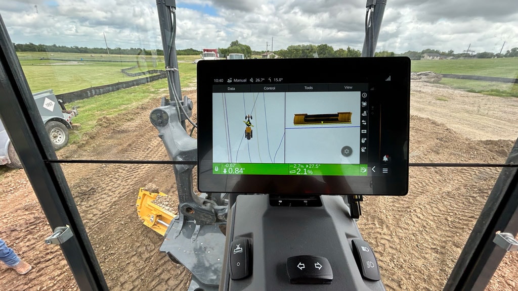 In-cab display guides a John Deere motor grader operator during grading on a construction site.