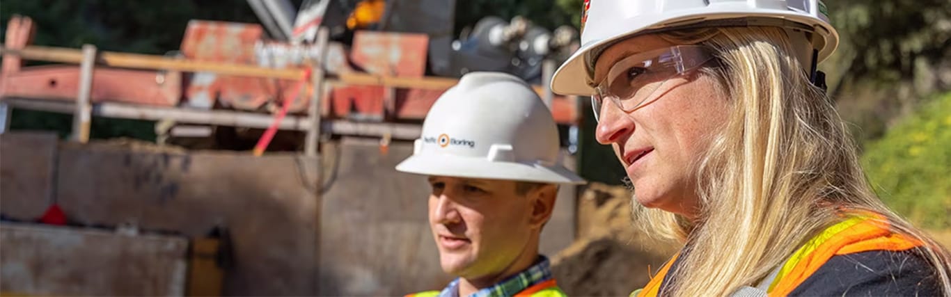 Male and female workers with construction hats on looking at a piece of construction equipment