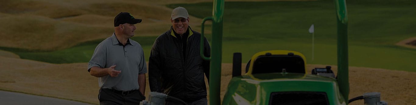 two people next to golf equipment with golf course in background