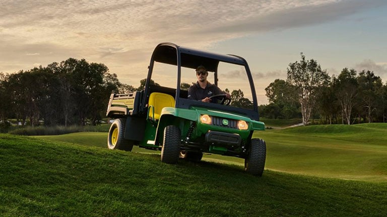 person riding gator vehicle on golf course at dusk