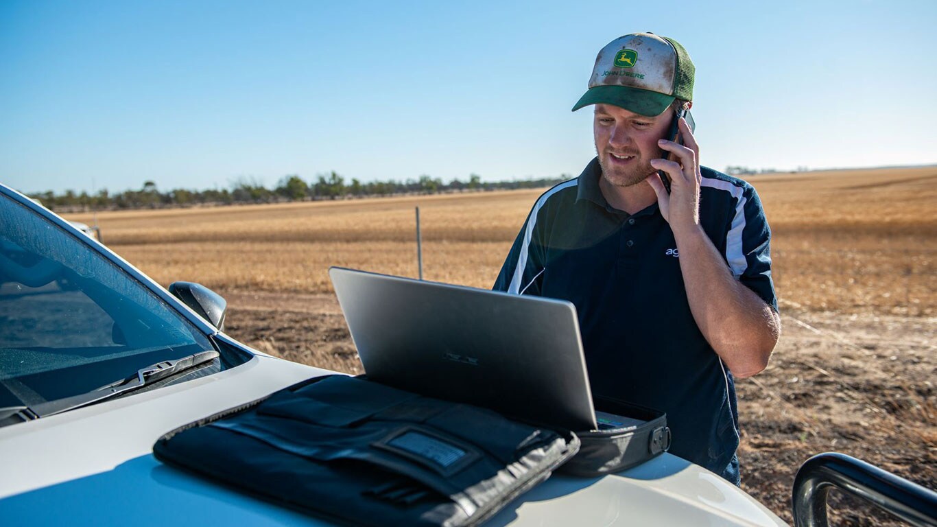 Man talking on mobile phone while working on laptop in field