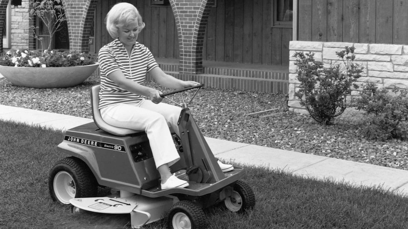 Historical black and white image of a lady on an old John Deere Mower