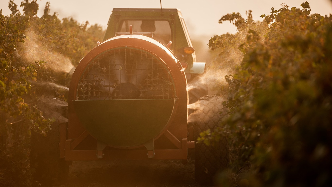 Smart Apply spraying chemicals to crops in a field during sunset.