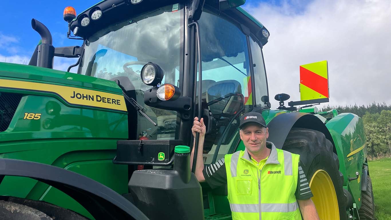 Bryce Dickinson leaning against a John Deere utility tractor.