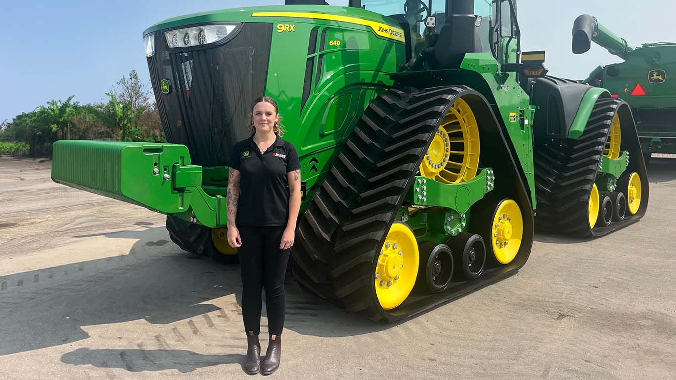 Mollie Clarke standing outside in front of a John Deere tractor with a blue sky in the background.