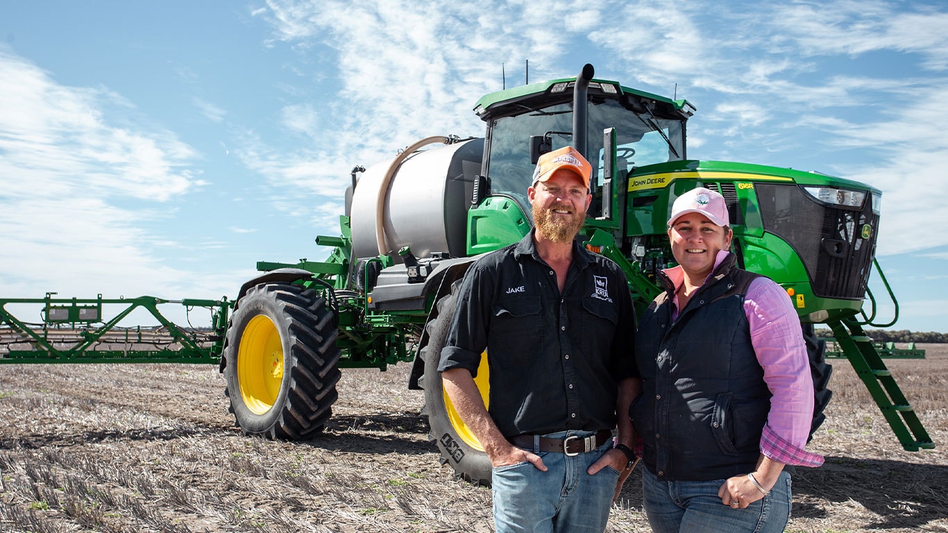 Jake and Felicity Hamilton in front of their John Deere Self-Propelled Sprayer in a field.