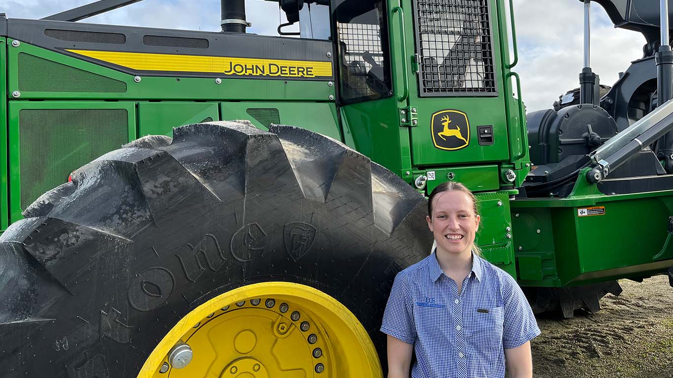 Paige Hunter smiling near the tire of a large John Deere machine outside.