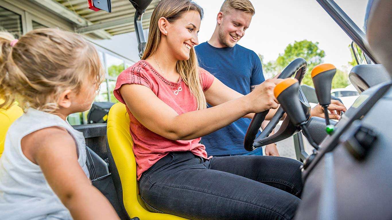 Young woman and child sit in the Gator utility vehicle while her husband observes and smiles.
