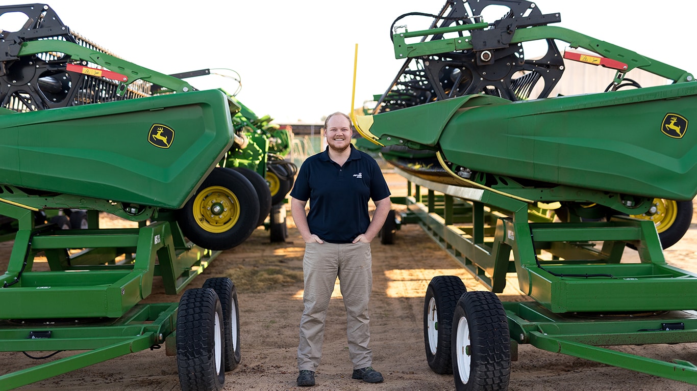 Caleb Dover is standing amongst large John Deere equipment outside the AFGRI Equipment dealership in Wongan Hills, north-east of Perth