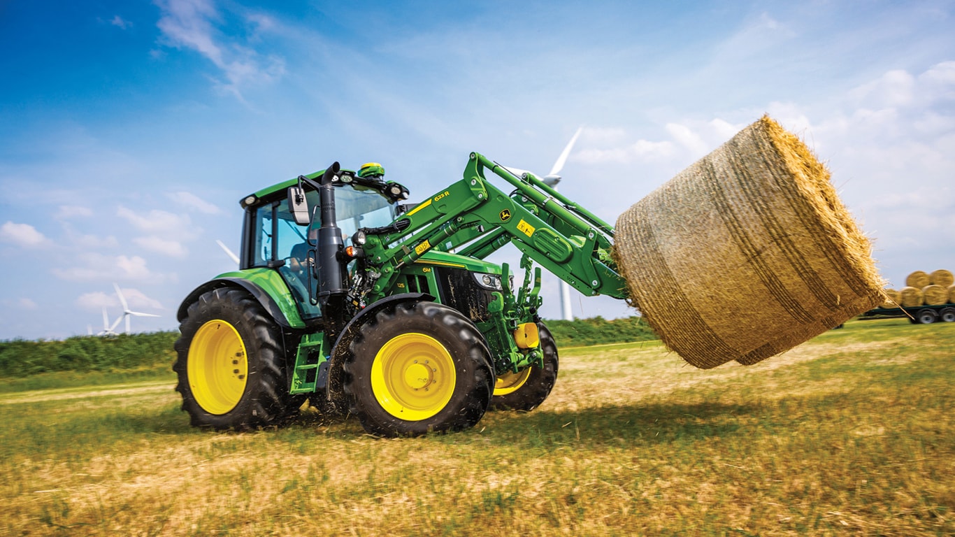 a 6M 125 tractor with a 623R hook picking up a bale of hay