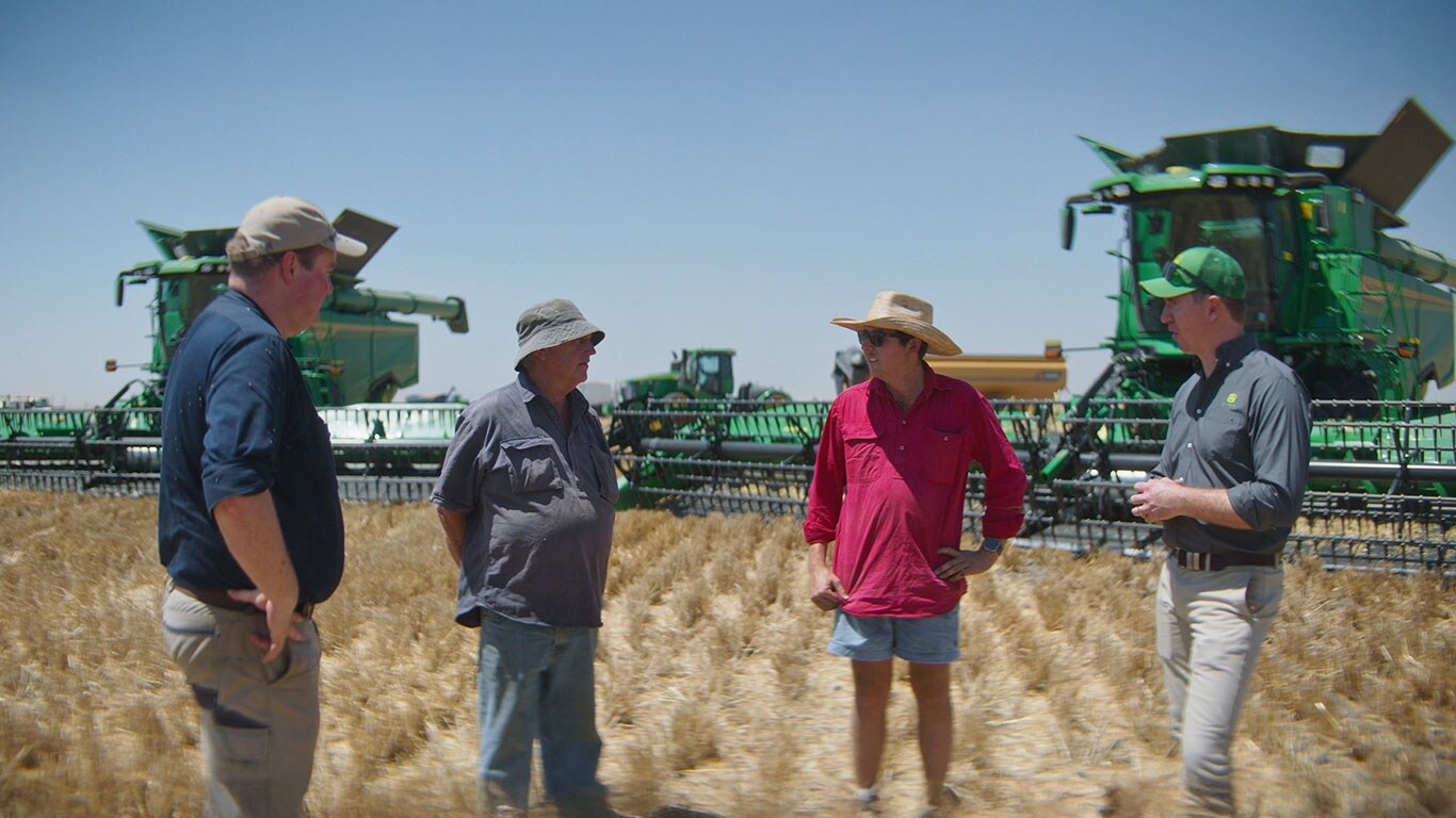 Four men standing in front of machinery in paddock.