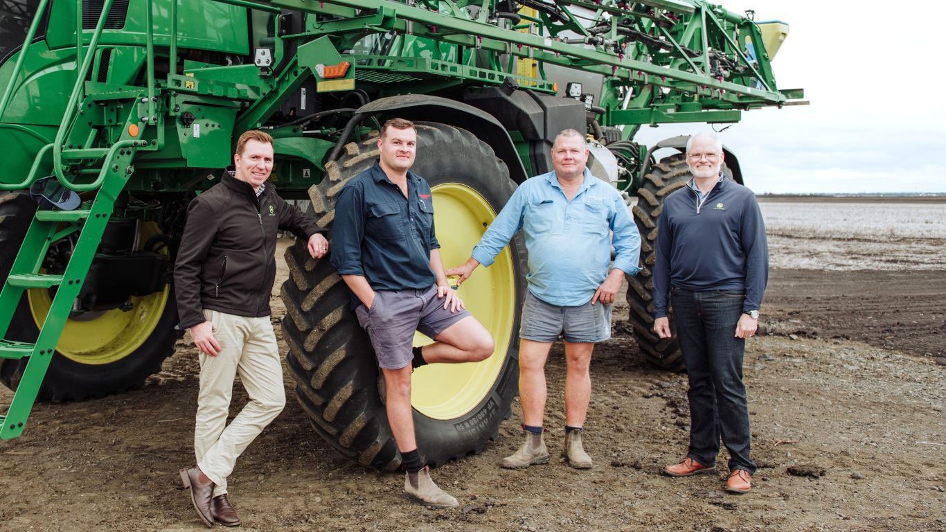 Four men standing next to farm machinery in a ploughed paddock.