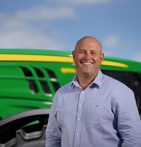 Smiling man stands in front of a tractor