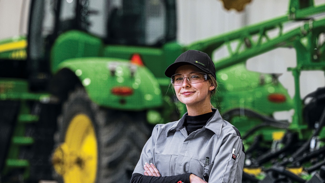 Grinning woman with arms crossed in front of tractor