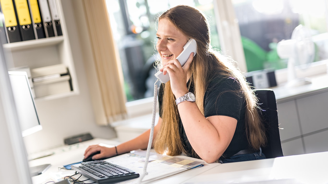 a woman at a desk smiling while on the phone