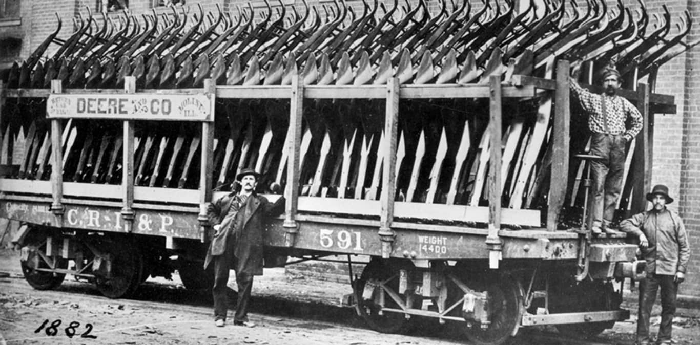 Gentlemen stand next to a trailer full of original plows