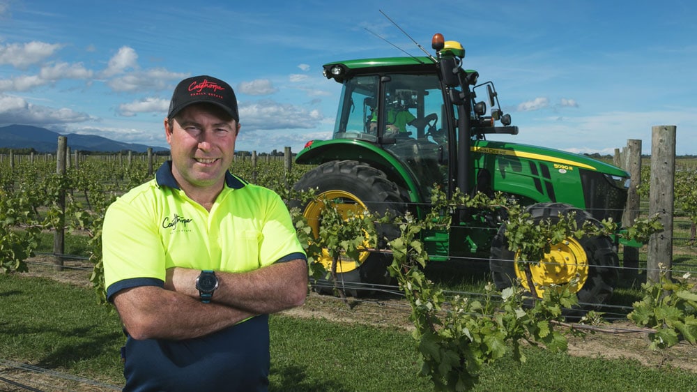 Man in front of John Deere tractor on his vineyard