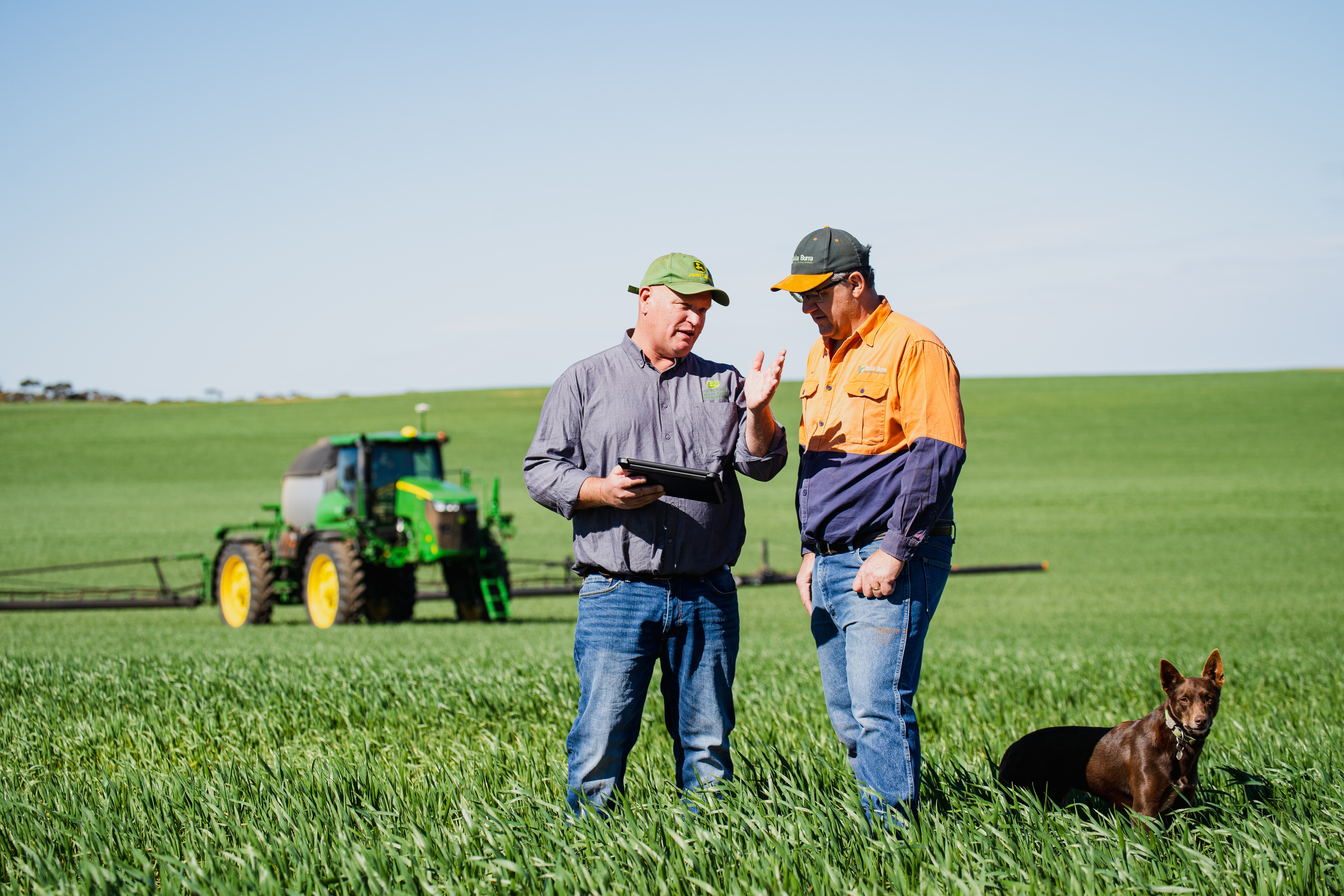 two farmers and their dog stand in a field with a tablet