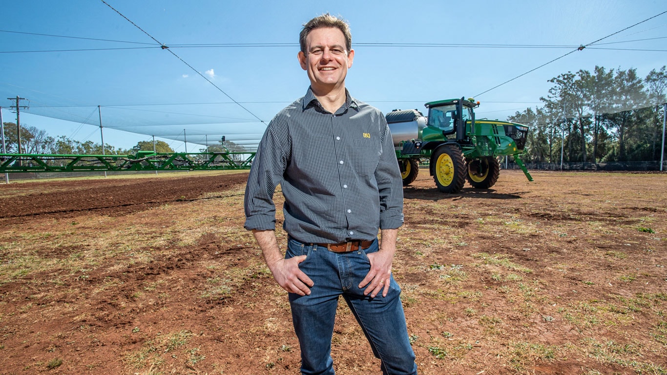 Photograph of a man in a field in front of John Deere equipment