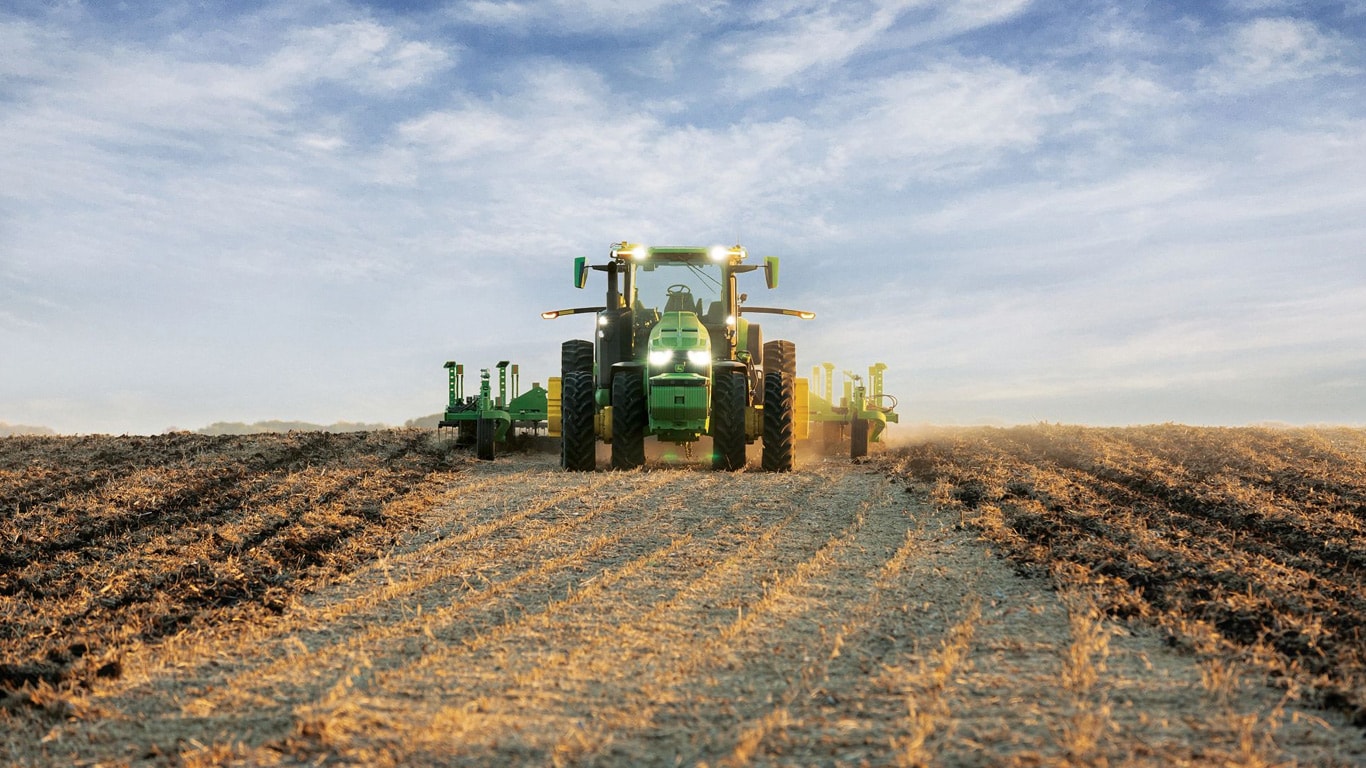 Self-driving John Deere tractor pulling tillage equipment through an open field.
