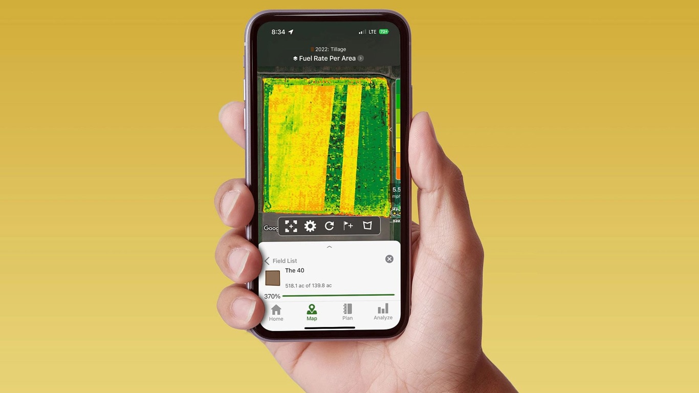 Hand holding a smart phone displaying a John Deere Operations Center with fuel rate data.