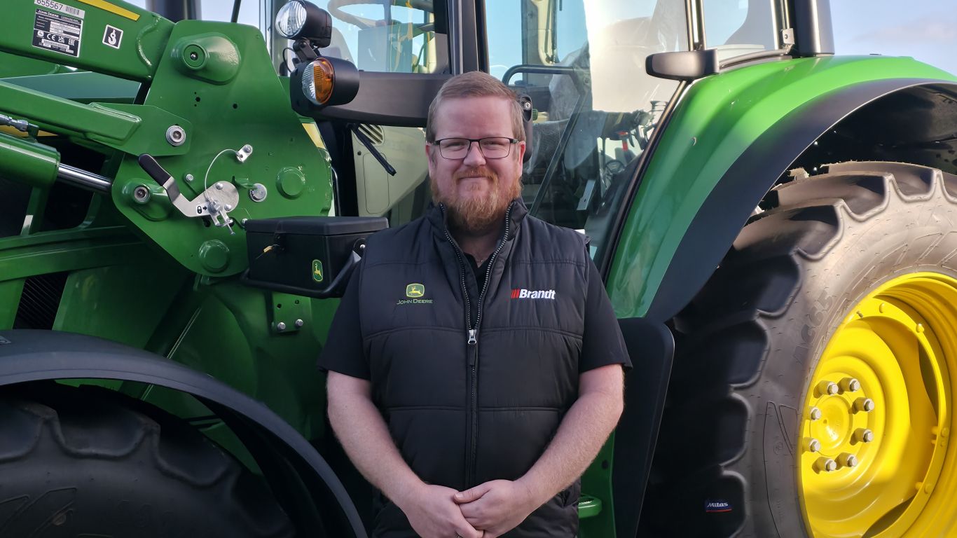 Person standing beside a John Deere tractor, with loader arm and large rear wheel visible.