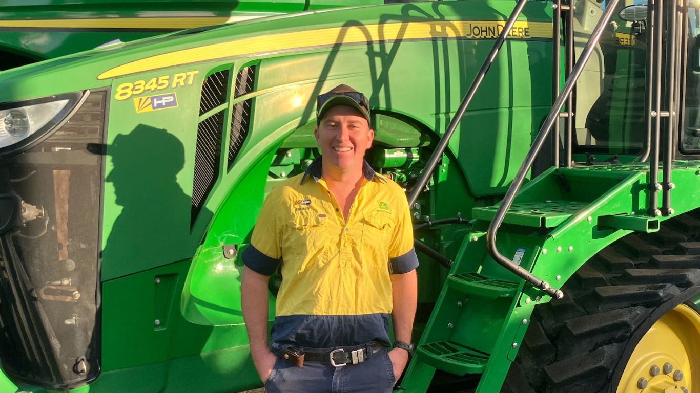 Person standing beside a John Deere 8345RT tractor in an outdoor equipment yard.