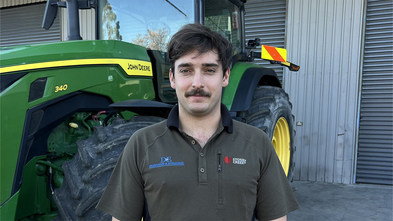 Person standing in front of a John Deere 340 tractor outside a farm equipment facility.