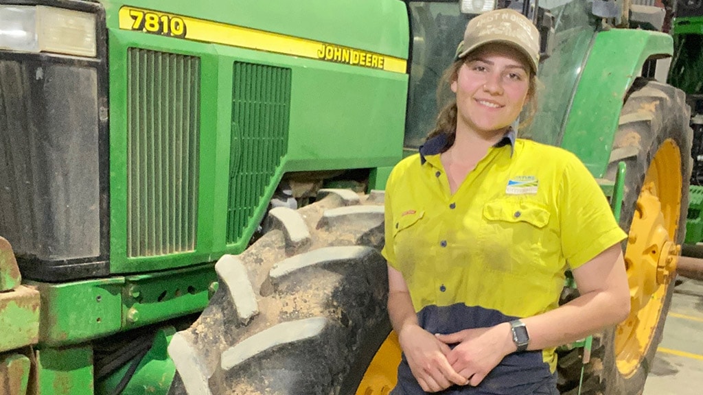 Jaymee smiling while standing in front of a Deere tractor