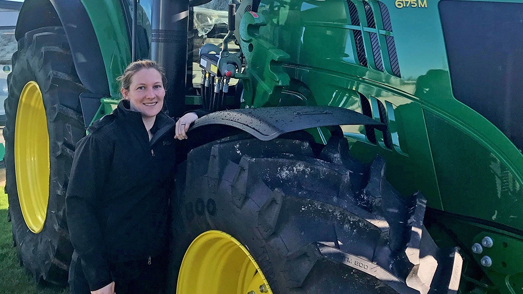 Megan smiling while leaning on a 6175M Deere tractor