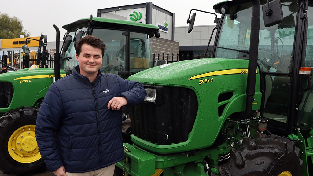 Mitch smiling and leaning on Deere tractor