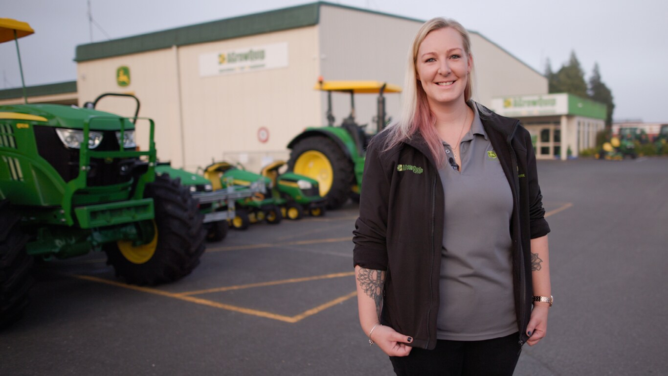 Cass smiling outside of a facility with Deere equipment lined up behind her