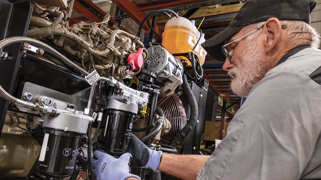 Person servicing engine components with filters, hoses, and wiring in a workshop setting.