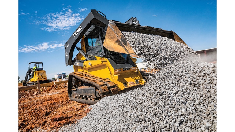 A 331G Compact Track Loader moving rocks at a worksite with a 35G Excavator in the background.