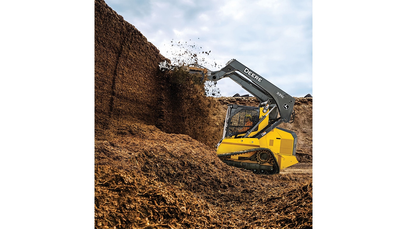 A 331G Compact Track Loader tearing down a wall of mulch and dirt with an AD7 silage defacer attachment.
