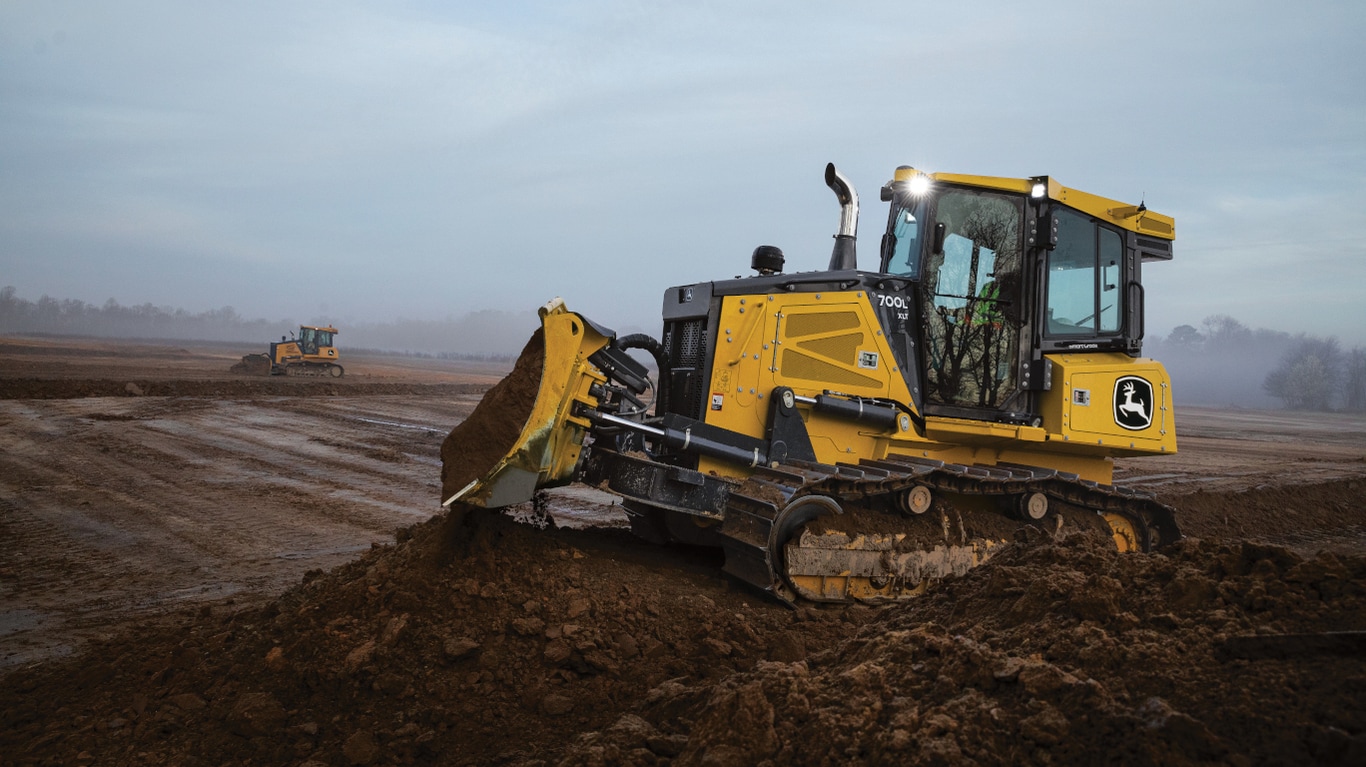 700L Dozer moving dirt at a worksite with headlights on during a cloudy day.