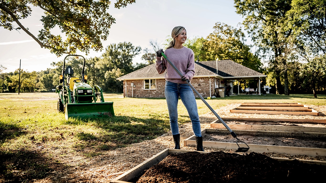 woman gardening with a Deere compact tractor in the background