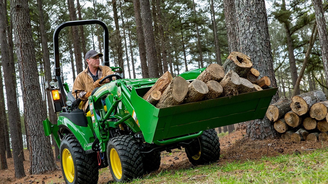 a man driving a tractor through woods hauling logs