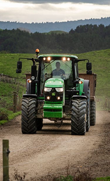 Tractor 6140M driving down a dirt road hauling a trailer