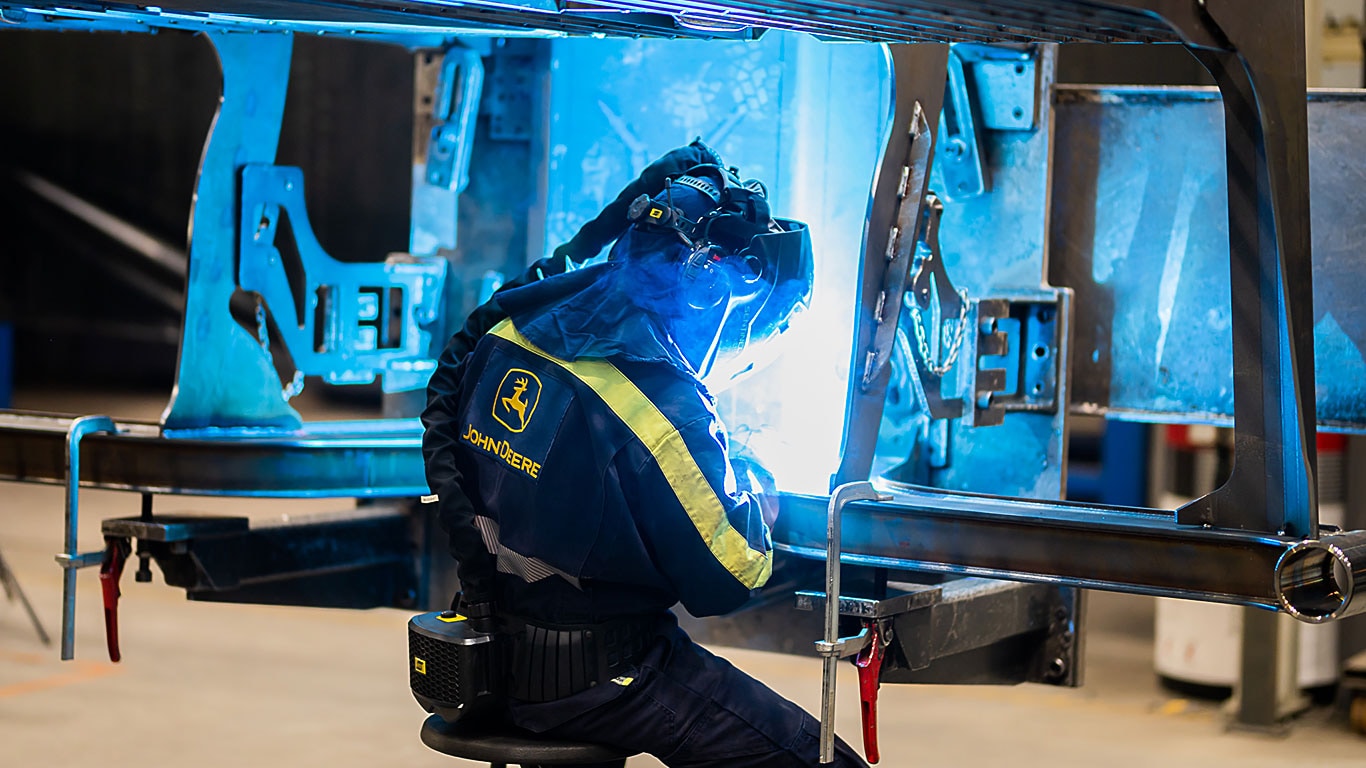 A person is welding a headboard of a forest machine