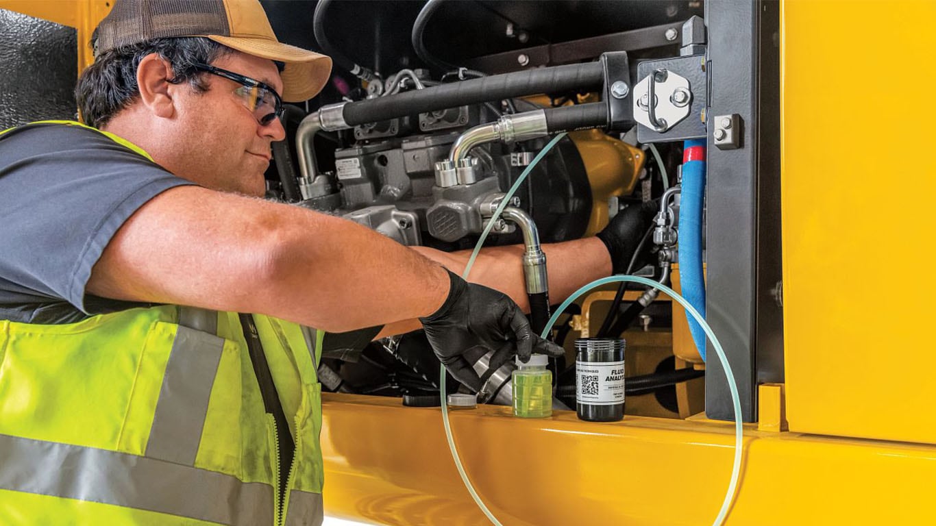 A service technician dressed hi-vis safety gear is undertaking an engine inspection of John&nbsp;Deere construction equipment. This includes an oil analysis which aims to drastically reduce catastrophic downtime, optimise drain intervals, and save our customers money.