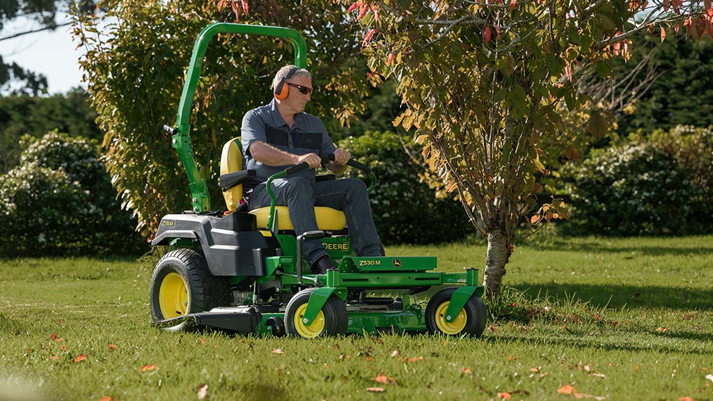 Person mowing lawn with John Deere Z530M near tree in garden using zero-turn mower.