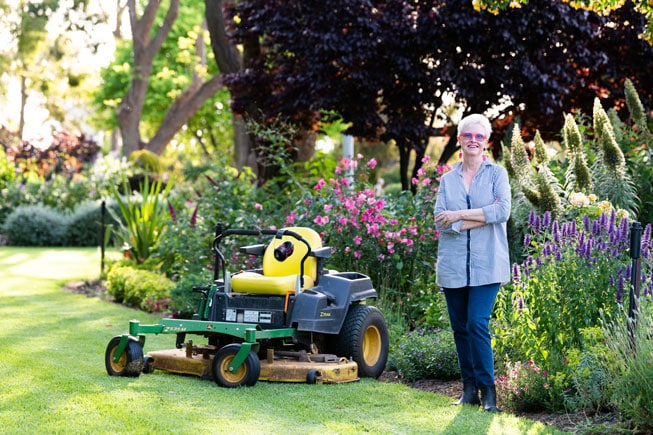 Julie Armstrong smiling with her arms crossed, standing in front of her garden