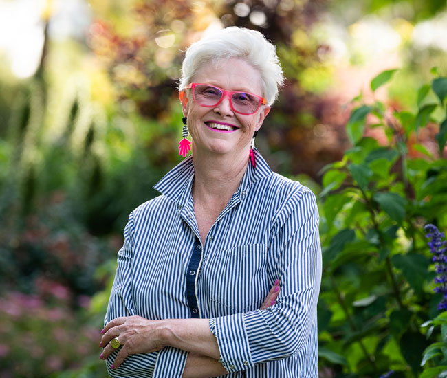 Julie Armstrong smiling with her arms crossed, standing in front of her garden