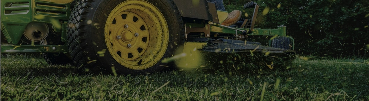 Close up image of the base of a John Deere lawn mower cutting grass.