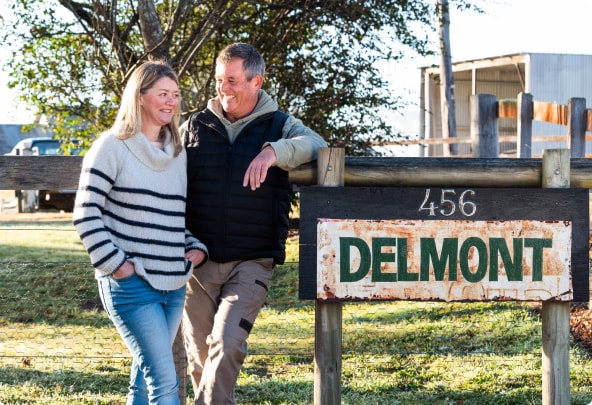 Sandy and Tim Palmer leaning against a sign that says 'Delmont'