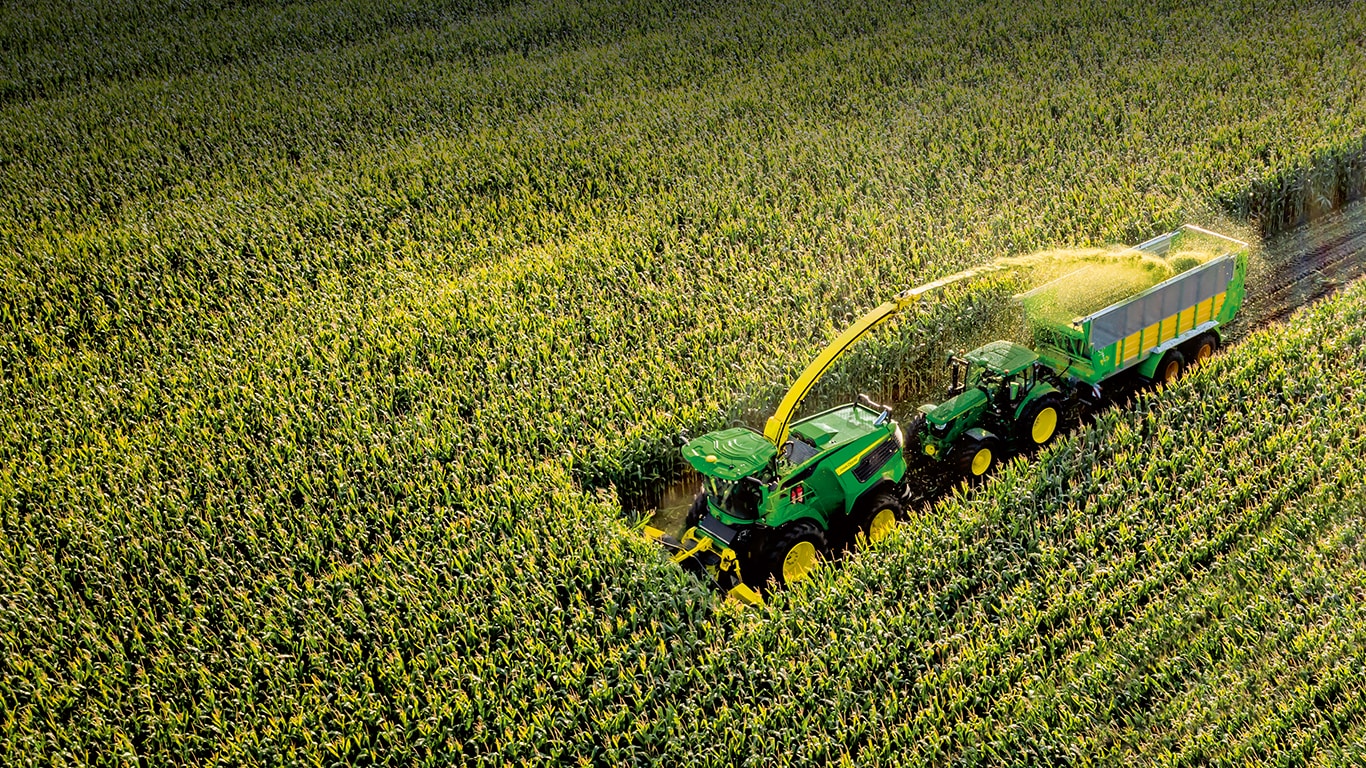 Green Self-Propelled Forage Harvester harvesting crop with green tractor
