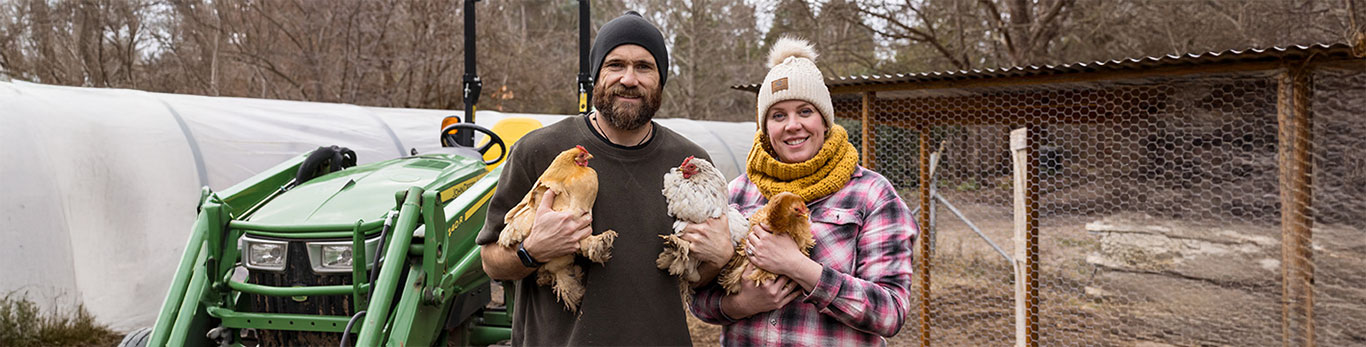Two people standing outdoors holding chickens next to a green tractor.
