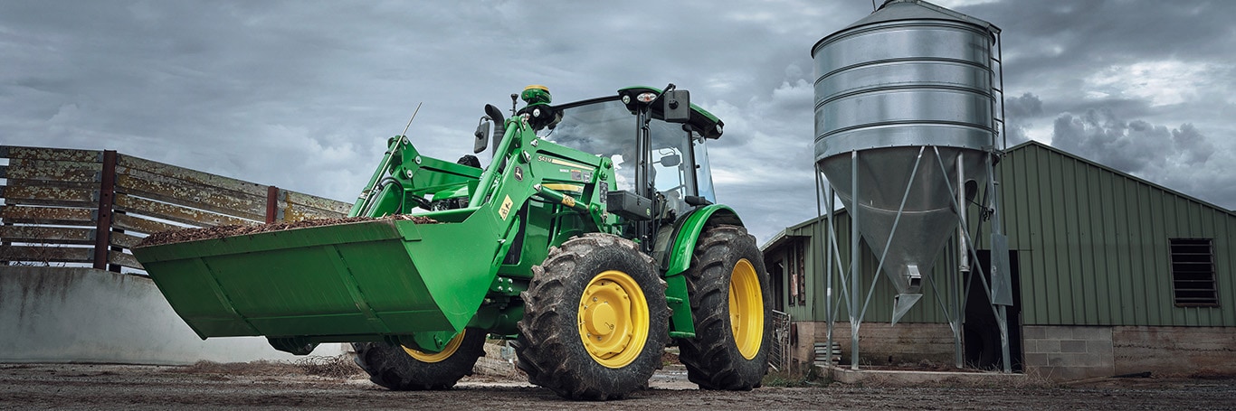 Tractor with loader in front of fence and farm equipment